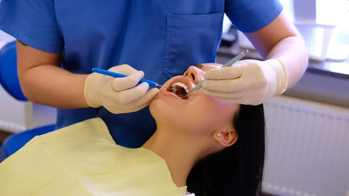 Dentist performing wisdom teeth removal on young woman using dental tools