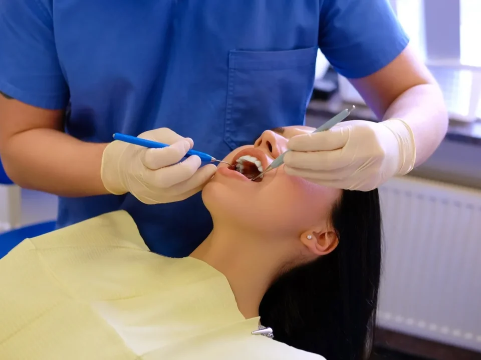 Dentist performing wisdom teeth removal on young woman using dental tools