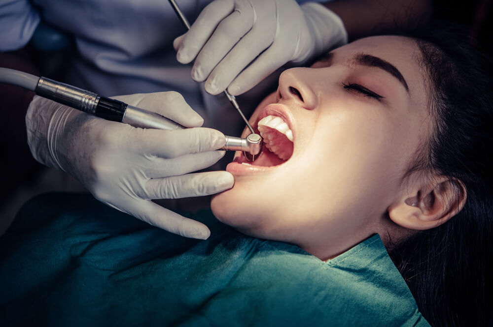 Woman undergoing teeth removal treatment at dental clinic with dentist using surgical instruments